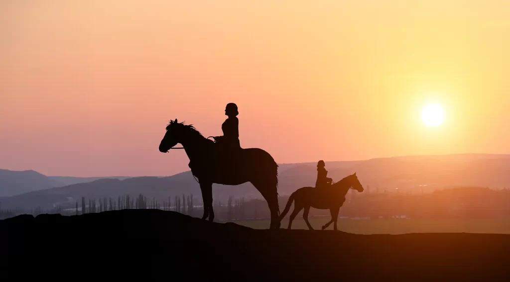 silhouettes of women on horseback against the setting sun