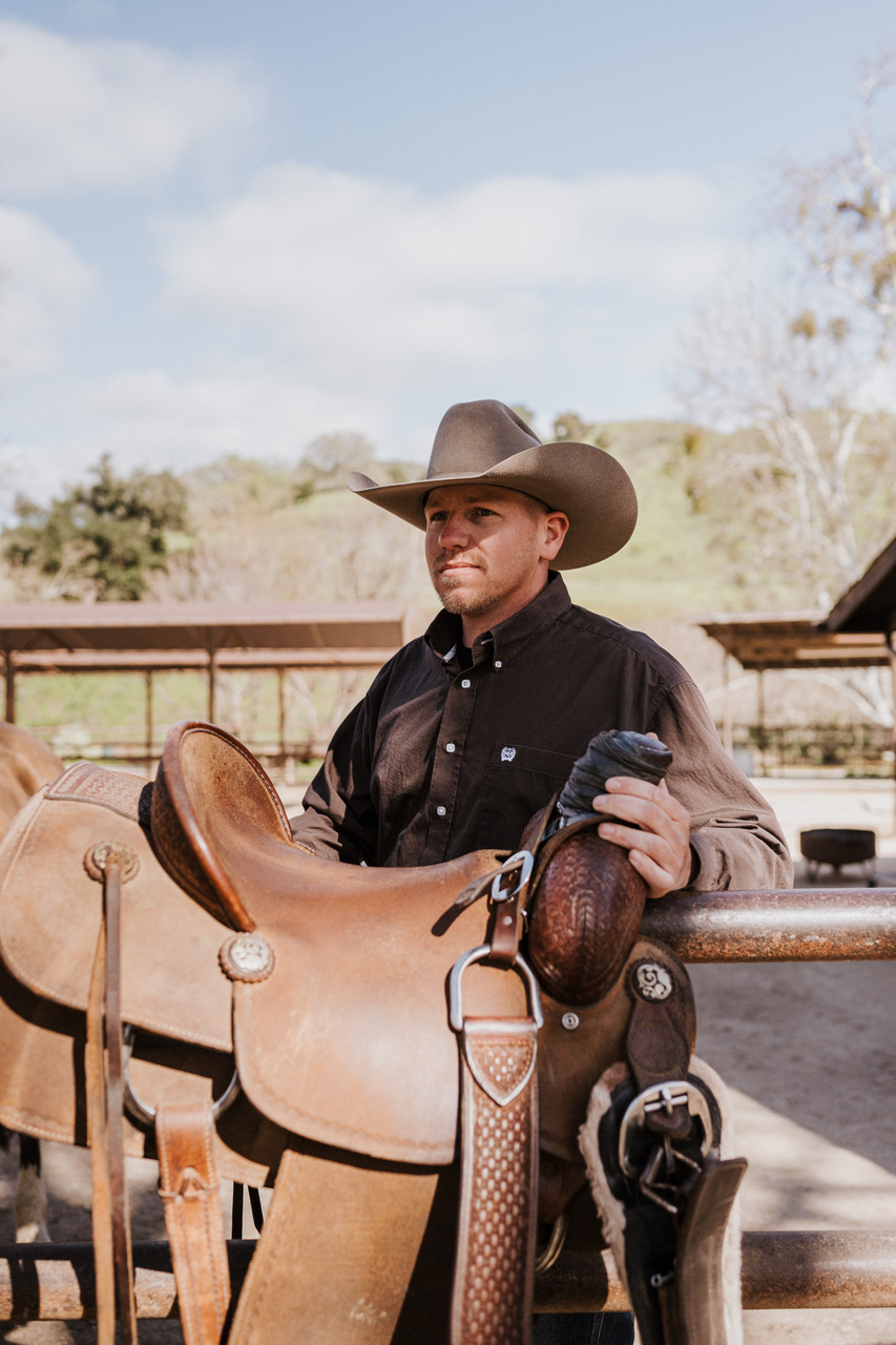 Brandon holding a saddle as he works to get horses ready to ride at the Women of the Rancho Retreat healing retreat
